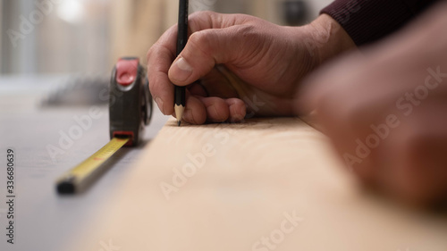 The carpenter measures the wooden board and marks it with a graphite pencil. Meter in the background