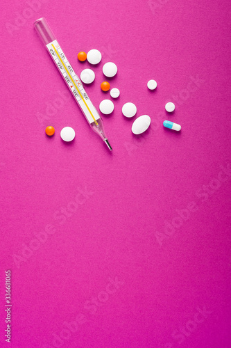 Pills, tablets and analog thermometer on pink purple background, healthcare medical concept, antibiotics and cure, top view copy space