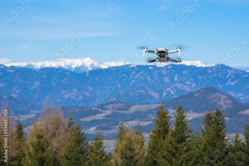 White drone with photo camera flying in the blue sky and beautiful mountain landscape in the background