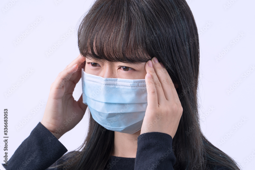 Young woman is feeling dizzy, headache, sick, unwell with wearing a medical blue face mask over the gray background, close up, copy space. Young woman is feeling dizzy, headache, sick, unwell with wearing a medical blue face mask over the gray background, close up, copy space.