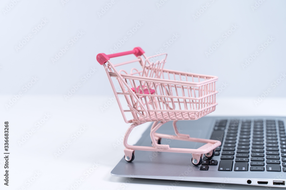 Online shopping. Mini empty pink shop cart trolley over a laptop computer on white table background, buying at home concept, close up