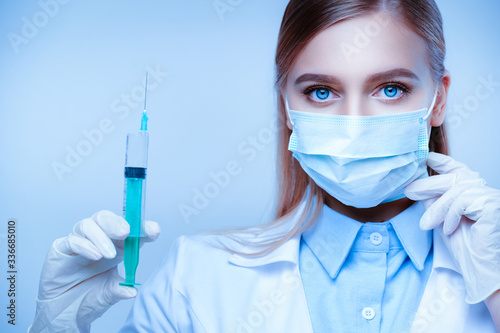 Portrait of female nurse with gloves holding syringe and touch her mask on white isolated background