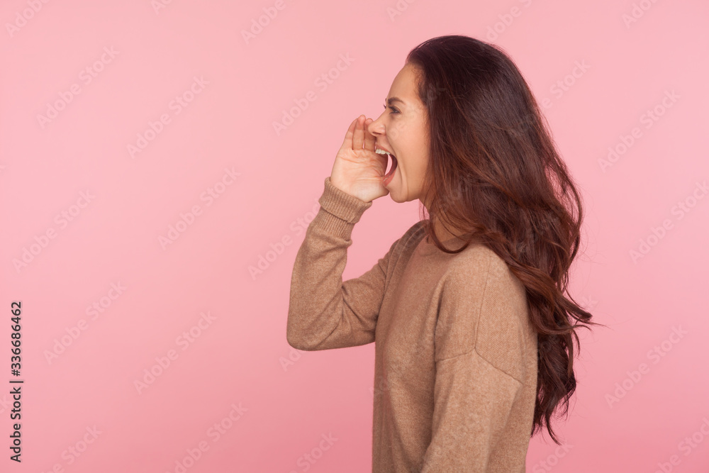 Attention, important message! Side view of young woman with brunette wavy hair shouting news or proclaiming idea with hand near mouth, announcing advertisement. studio shot isolated on pink background Attention, important message! Side view of young woman with brunette wavy hair shouting news or proclaiming idea with hand near mouth, announcing advertisement. studio shot isolated on pink background