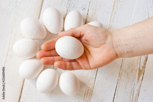 A white chicken egg lying in a man’s hand, shot on a white painted wooden surface. Background for livestock products.
