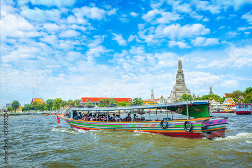 View over river Chao Phraya from boat back to temple Wat Arun, eldest temple in Bangkok. In foreground is speed longboat passing. Behind are tour boats and ferries. 