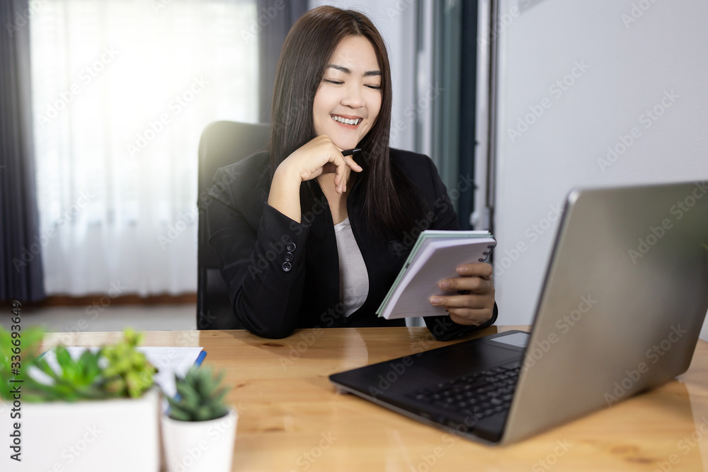 Asian woman working Holding a pen and notebook in home with laptop computer smile and happy work. Work from home concept. Asian woman working Holding a pen and notebook in home with laptop computer smile and happy work. Work from home concept.