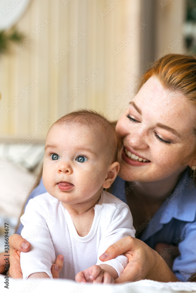 A young mother hugs and caresses a three-month-old baby in bed. Moments of happy motherhood A young mother hugs and caresses a three-month-old baby in bed. Moments of happy motherhood