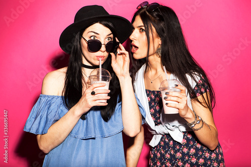 Wall Mural Two caucasian brunette hipster woman in casual stylish outfit having fun drinking milkshakes with straws