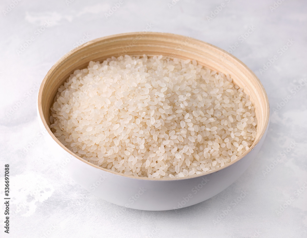 Raw rice in a bamboo bowl on a concrete background.