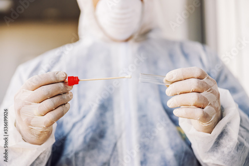 Man in protective suit with mask holding sample buccal cotton swab and test tube ready to collect DNA from the cells. Coronavirus covid-19. Infection prevention and control of epidemic. photo