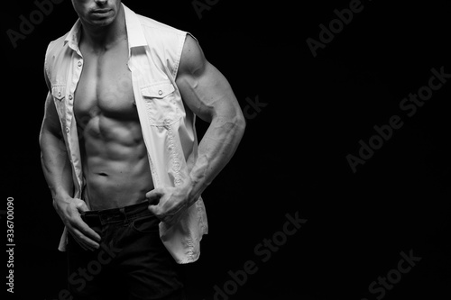Sexy torso. Fashion portrait of sporty healthy strong muscle guy. Muscular model sports young man in jeans showing his press on a black background. Black and white photography 