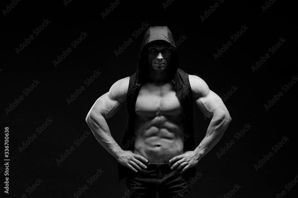 Muscular model sports young man in jeans showing his press on a black background. Fashion portrait of sporty healthy strong muscle guy. Sexy torso.  Black and white photography
