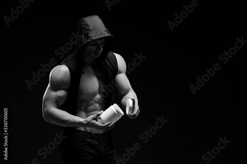 Muscular bodybuilder with jar of protein on a dark background. Sports nutrition. Bodybuilding nutrition supplements, sport, workout, healthy lifestyle concept. Black and white photography