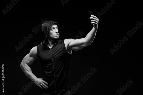 Muscular bodybuilder with phone in hands on a dark background. Sports nutrition. Bodybuilding nutrition supplements, sport, workout, healthy lifestyle concept. Black and white photography