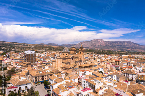 Aerial Drone photo of a beautiful city in a Almeria, Andalucia, Spain called Velez Rubio with red and orange house roof tops and a beautiful cathedral in the heart of the town with blue sky & mountain