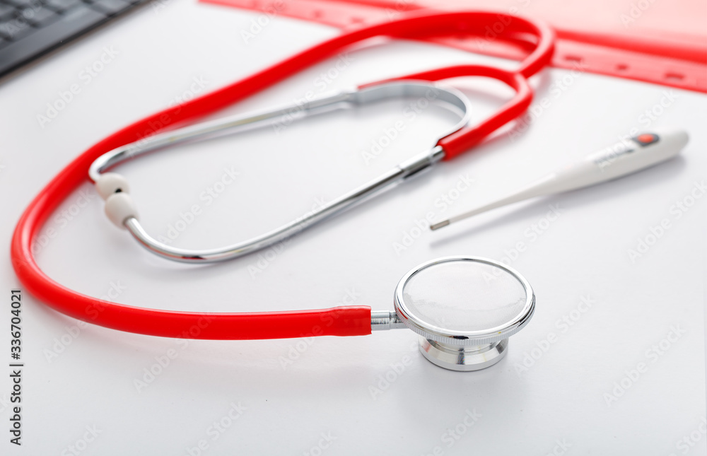 Medical thermometer red stethoscope on white table. Doctors professional equipment on workspace. Healthcare medical concept. Doctor appointment. Coronovirus Covid-19 prevention Medical thermometer red stethoscope on white table. Doctors professional equipment on workspace. Healthcare medical concept. Doctor appointment. Coronovirus Covid-19 prevention