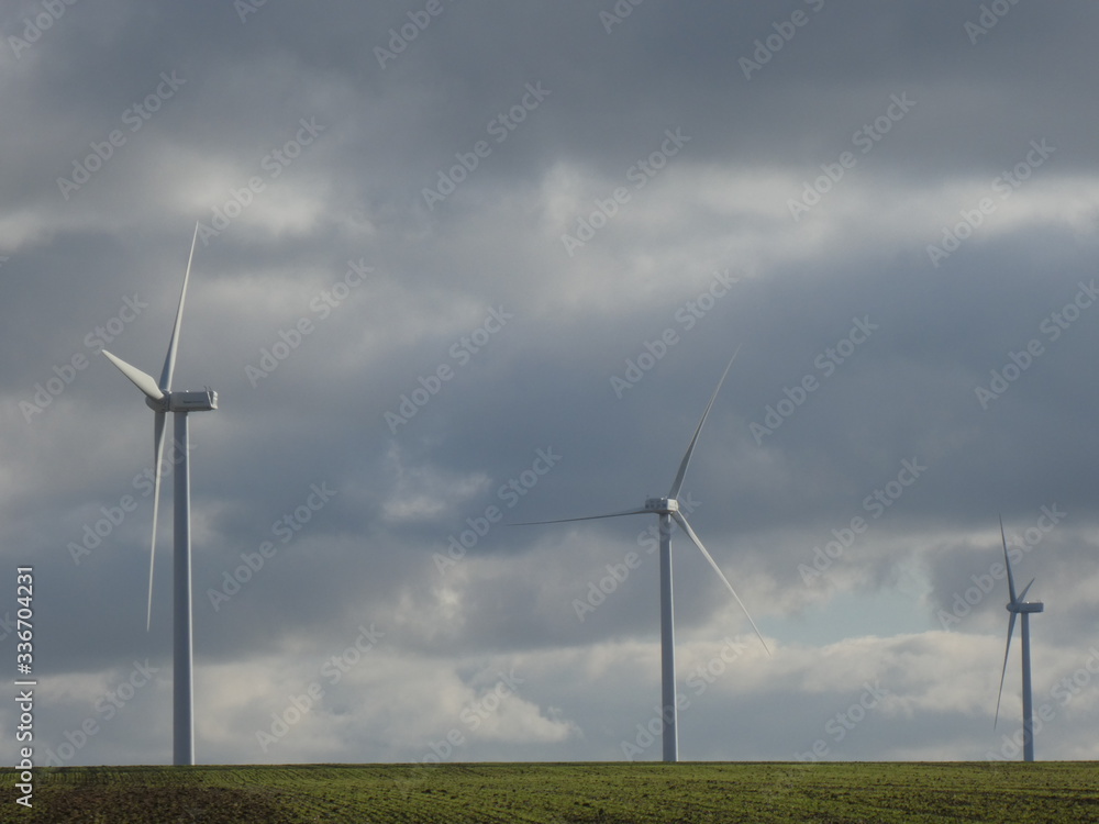 Row of three wind turbines in a green field with a cloudy sky in the background Row of three wind turbines in a green field with a cloudy sky in the background
