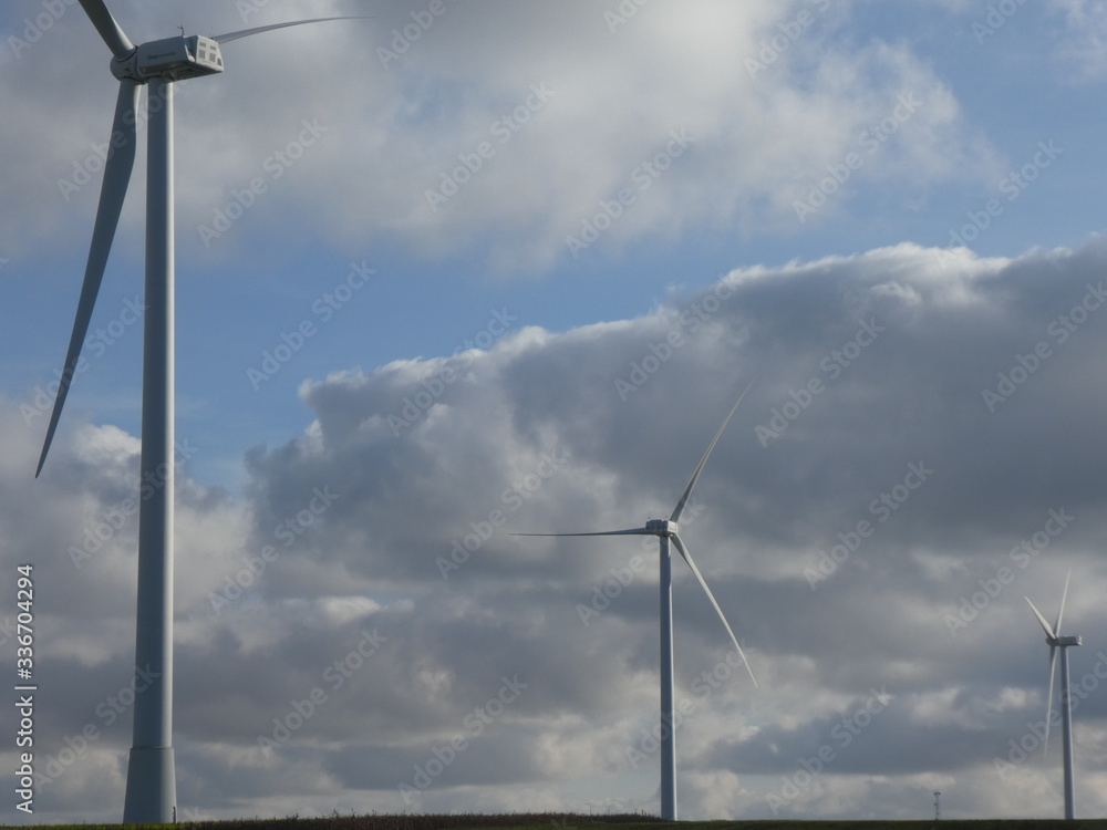 Three wind turbines aligned surrounded by cottony clouds in a blue sky