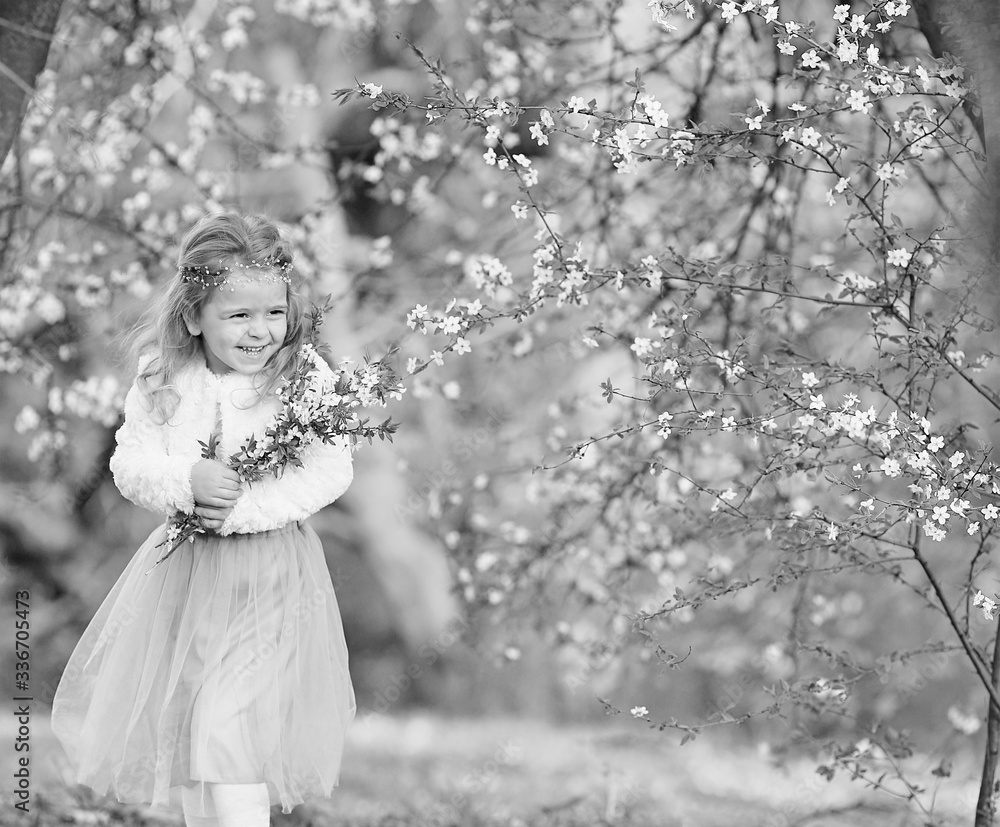 Stunning black and white portrait little girl laughs and has fun in a flying skirt and a fur blouse with a bouquet of blossoming cherry flowers in a spring garden. Daughter's day. Easter Stunning black and white portrait little girl laughs and has fun in a flying skirt and a fur blouse with a bouquet of blossoming cherry flowers in a spring garden. Daughter's day. Easter