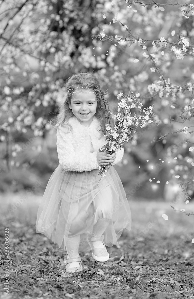 Stunning black and white portrait little girl laughs and has fun in a flying skirt and a fur blouse with a bouquet of blossoming cherry flowers in a spring garden. Daughter's day. Easter