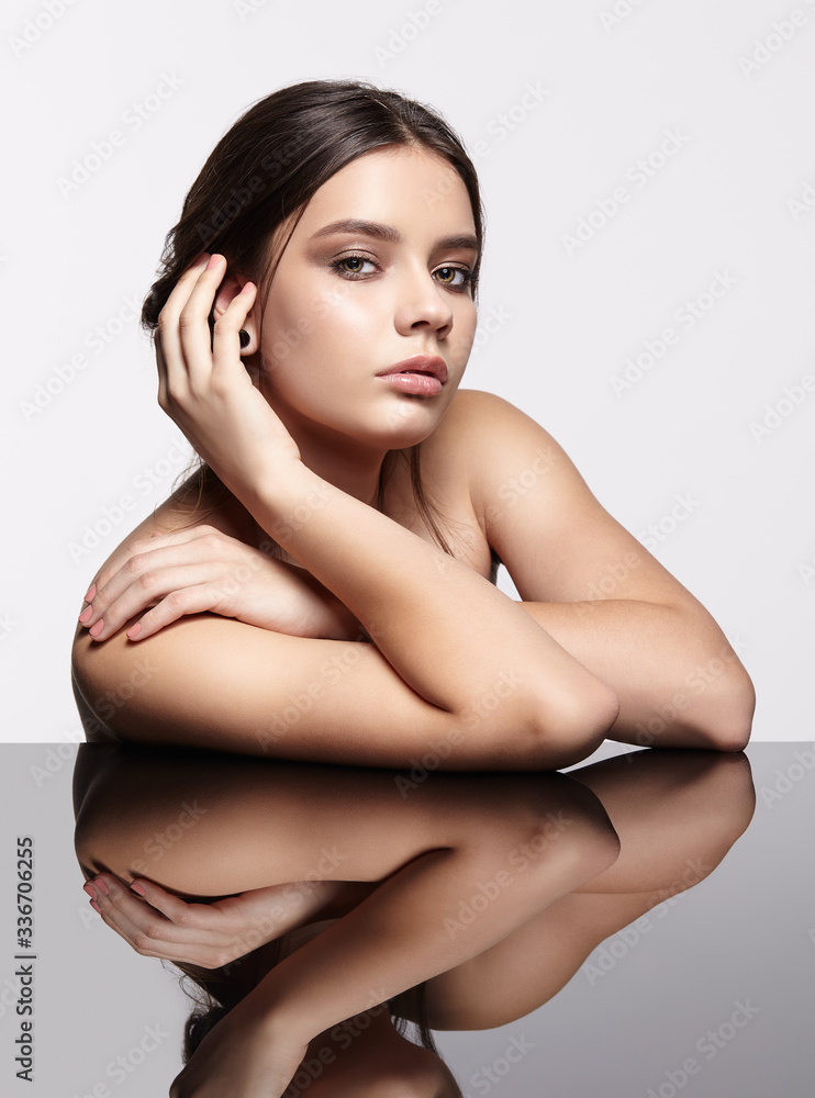 Fototapeta premium Portrait of young beautiful woman at reflecting table on gray background