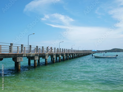 People go along the pier. A white longtail boat moored on the water near to the pier. Landscape of tourist Thailand. Cruise. Panoramic views of the sea, pier and tropical islands.