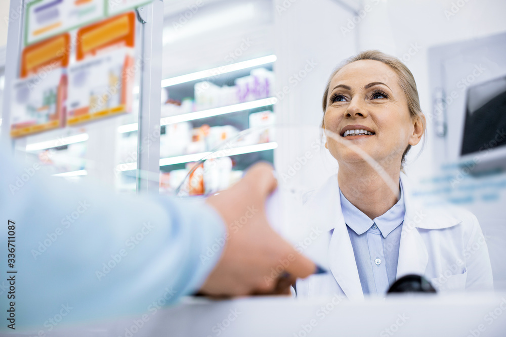 Jovial young female pharmacist selling drug in a drugstore