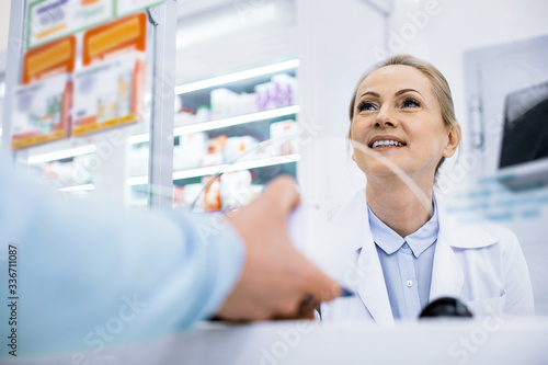 Jovial young female pharmacist selling drug in a drugstore