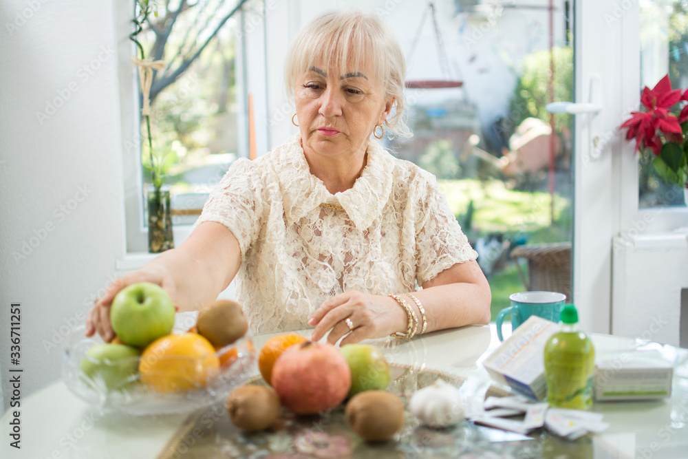 Senior woman taking apple from a fruit bowl instead of taking drugs at home. Nutrition and healthy food concept Senior woman taking apple from a fruit bowl instead of taking drugs at home. Nutrition and healthy food concept