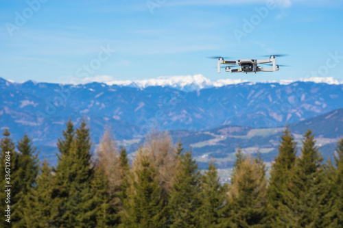 White drone with photo camera flying in the blue sky and beautiful mountain landscape in the background