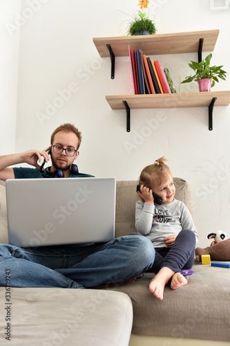 Dad working from home on his computer while his daughter is playing next to him.