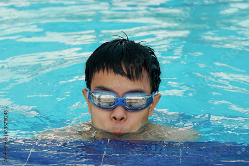 Asian young man wear goggles swim at outdoor swimming pool, eyes looking straight ahead prepared breath diving.
