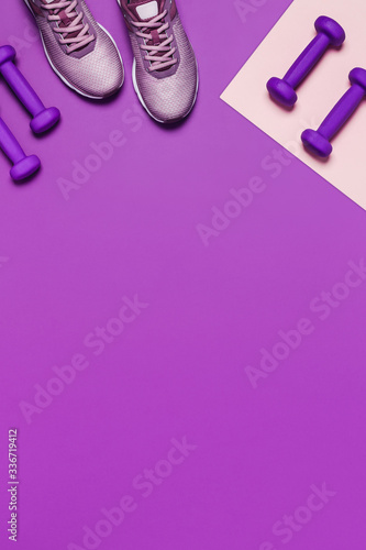 Sports flat-lay with sneakers, dumbbells and headphones on purple background. Vertical picture.