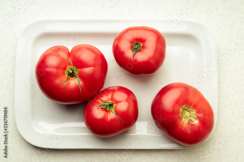 Four ripe fresh tomatoes on white plate, top view
