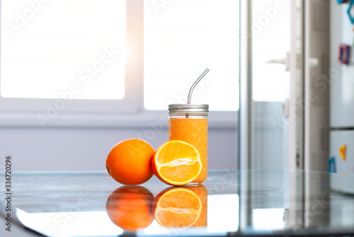 Fruit oranges and orange juice at the kitchen interior and transparent glass table on the light rays white background