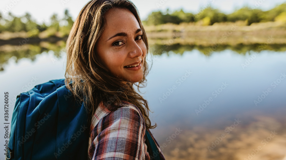 Female camper standing by the lake - obrazy, fototapety, plakaty 