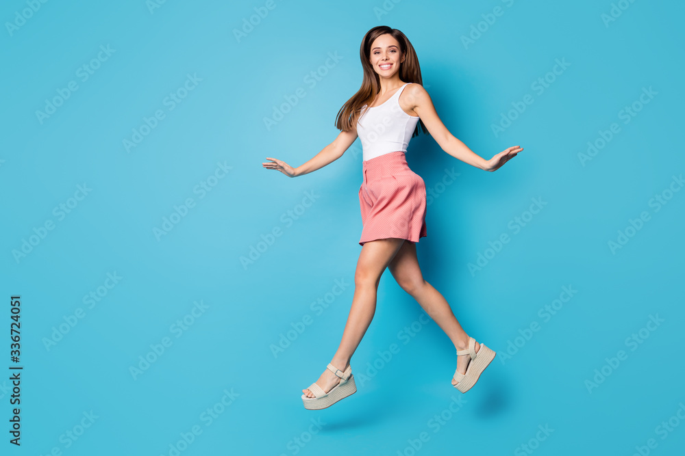 Full length profile side photo of content candid cute sweet girl jump have spring time weekend walk wear stylish clothes shoes isolated over blue color background Full length profile side photo of content candid cute sweet girl jump have spring time weekend walk wear stylish clothes shoes isolated over blue color background