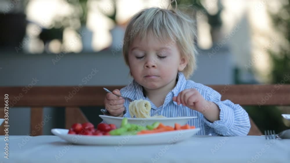 Cute child, toddler blond boy, eating spaghetti in garden summertime Cute child, toddler blond boy, eating spaghetti in garden summertime