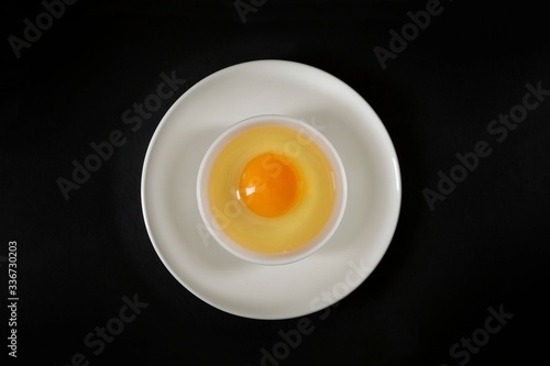 Aerial view of an egg: on a white plate another plate, inside, an egg white and an egg yolk, all on a black background