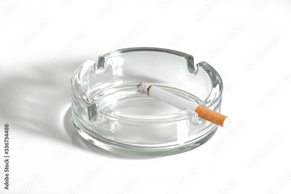 Cigarette lit in glass ashtray on white Cigarette lit in glass ashtray on white