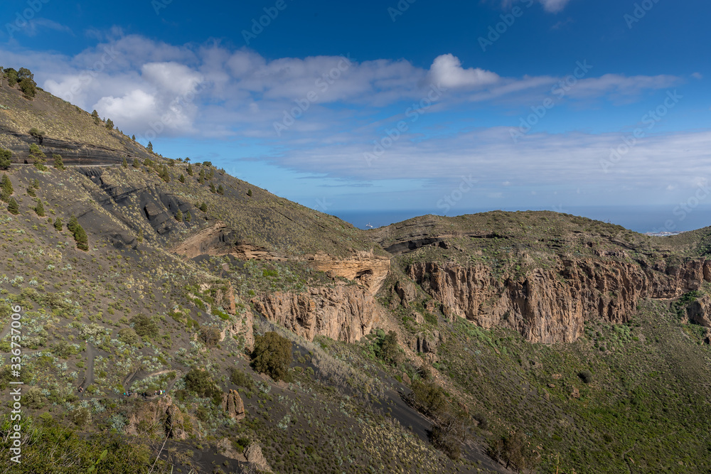 View of the mountainous landscape of volcanic origin along with lots of trees and vegetation and on the horizon, you can see the setting moon Gran Canary island