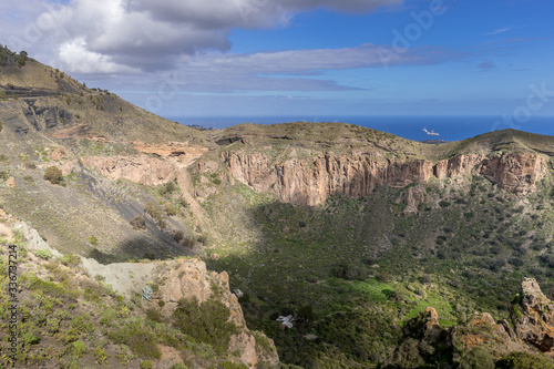 View of the mountainous landscape of volcanic origin along with lots of trees and vegetation and on the horizon  you can see the setting moon Gran Canary island