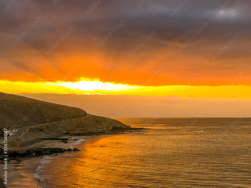 Sunrise from a cliff with moving clouds in a different direction forming a line where the sun rises on the sea and forms rays reflecting on the ocean surface from the Grand Canary.