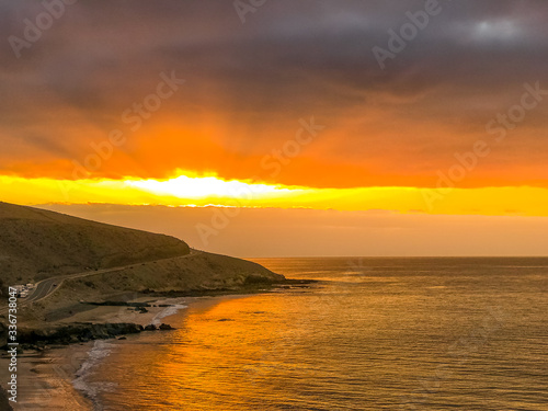 Sunrise from a cliff with moving clouds in a different direction forming a line where the sun rises on the sea and forms rays reflecting on the ocean surface from the Grand Canary.