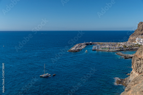 View from the air on the coast and bay in the city of Mogan on the Canary Islands where the bay harbor and people walking along the waterfront inside city