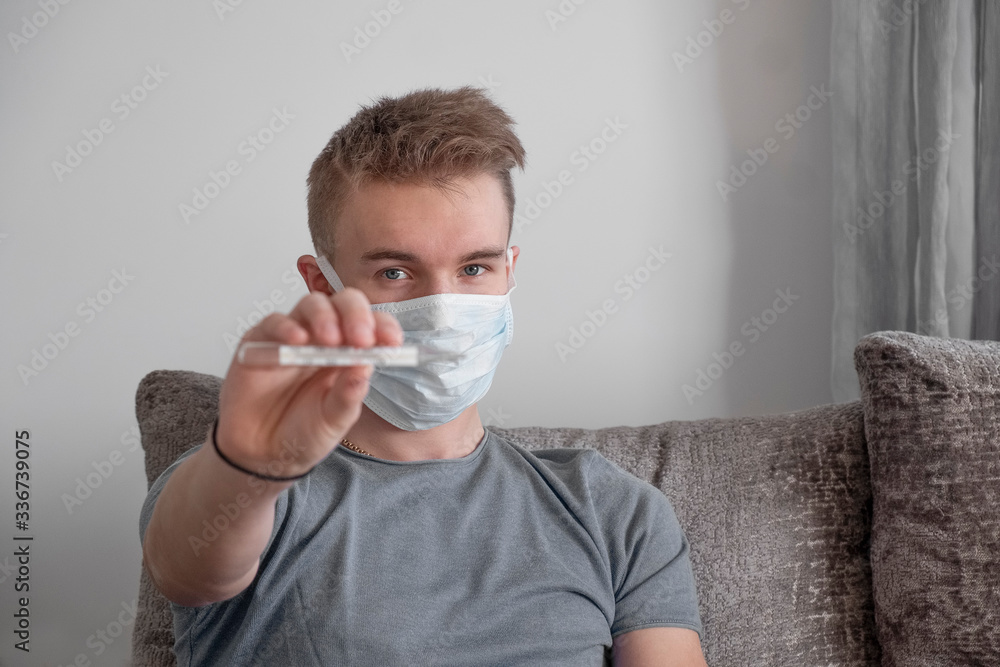 Young man in medical mask holding a thermometer. Quarantine. COVID-19 Young man in medical mask holding a thermometer. Quarantine. COVID-19