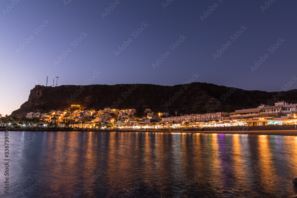 Obraz premium Mogan beach during sunset with the city lit up by street lights and freshly lit streets of the grand canary island valley