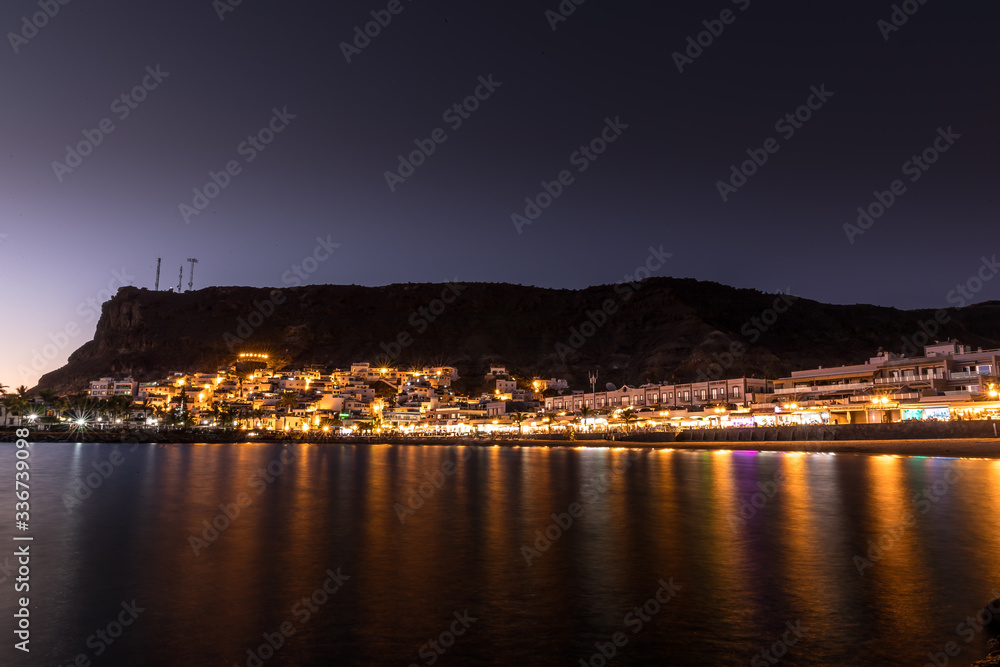 Mogan beach during sunset with the city lit up by street lights and freshly lit streets of the grand canary island valley