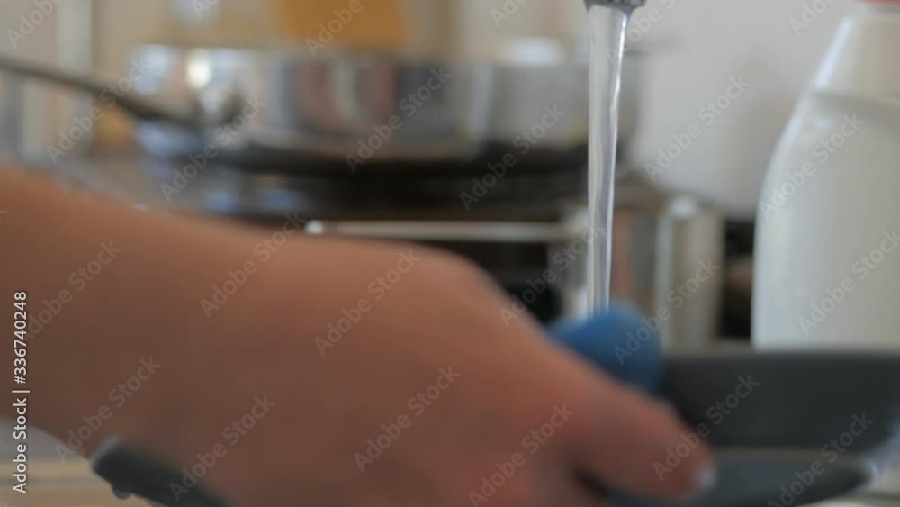 Closeup of a woman's hands washing dishes in the kitchen under a stream of water Closeup of a woman's hands washing dishes in the kitchen under a stream of water