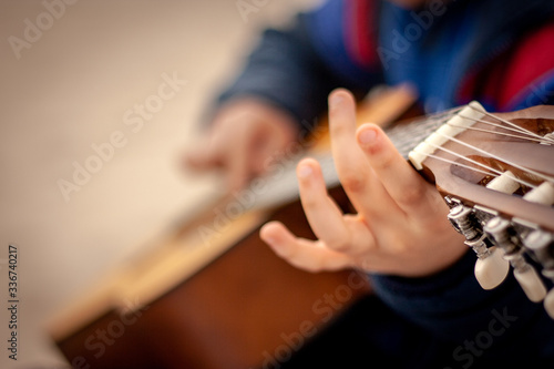 Detail of a young boy's hand playing a guitar on a beach